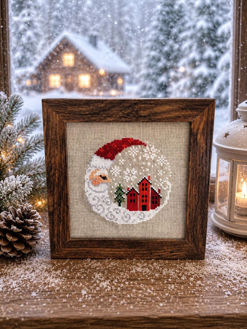 Framed cross-stitch — Santa Christmas Village, rustic wooden frame on wooden surface