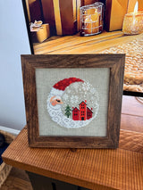 Framed cross-stitch — Santa Christmas Village, brown frame detail view